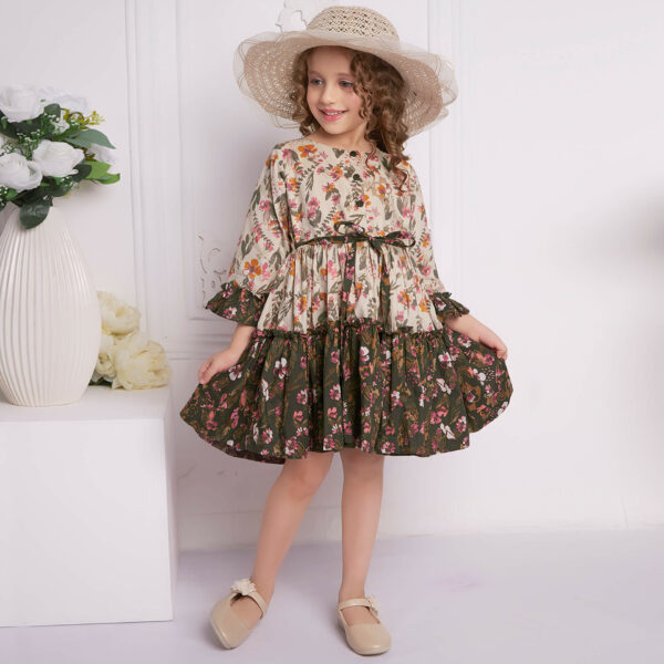 Posing in a beige and green ruffle dress, the girl playfully stretches the skirt with both hands