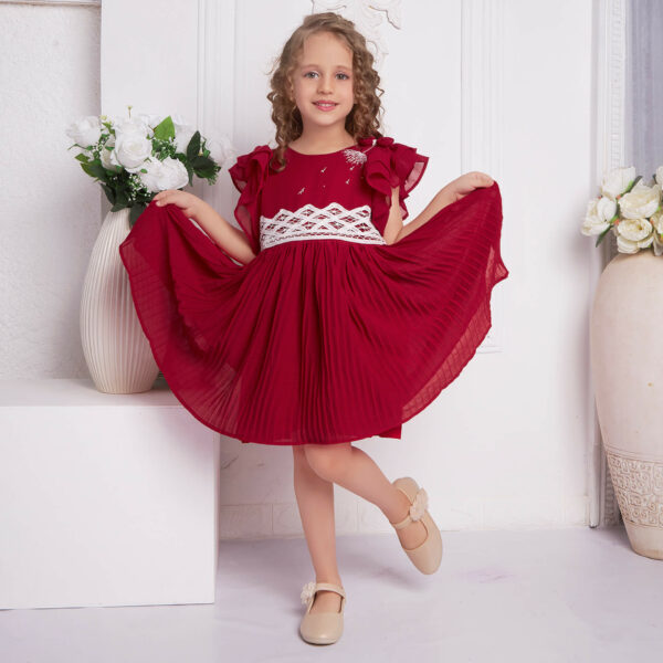 Posing in an embroidered red chiffon battenburg lace dress, the girl playfully stretches the skirt with both hands
