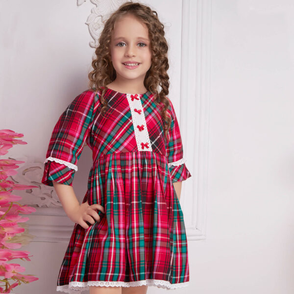 Posing straight, a girl wears a red plaid dress with white lace and red satin bows as trims