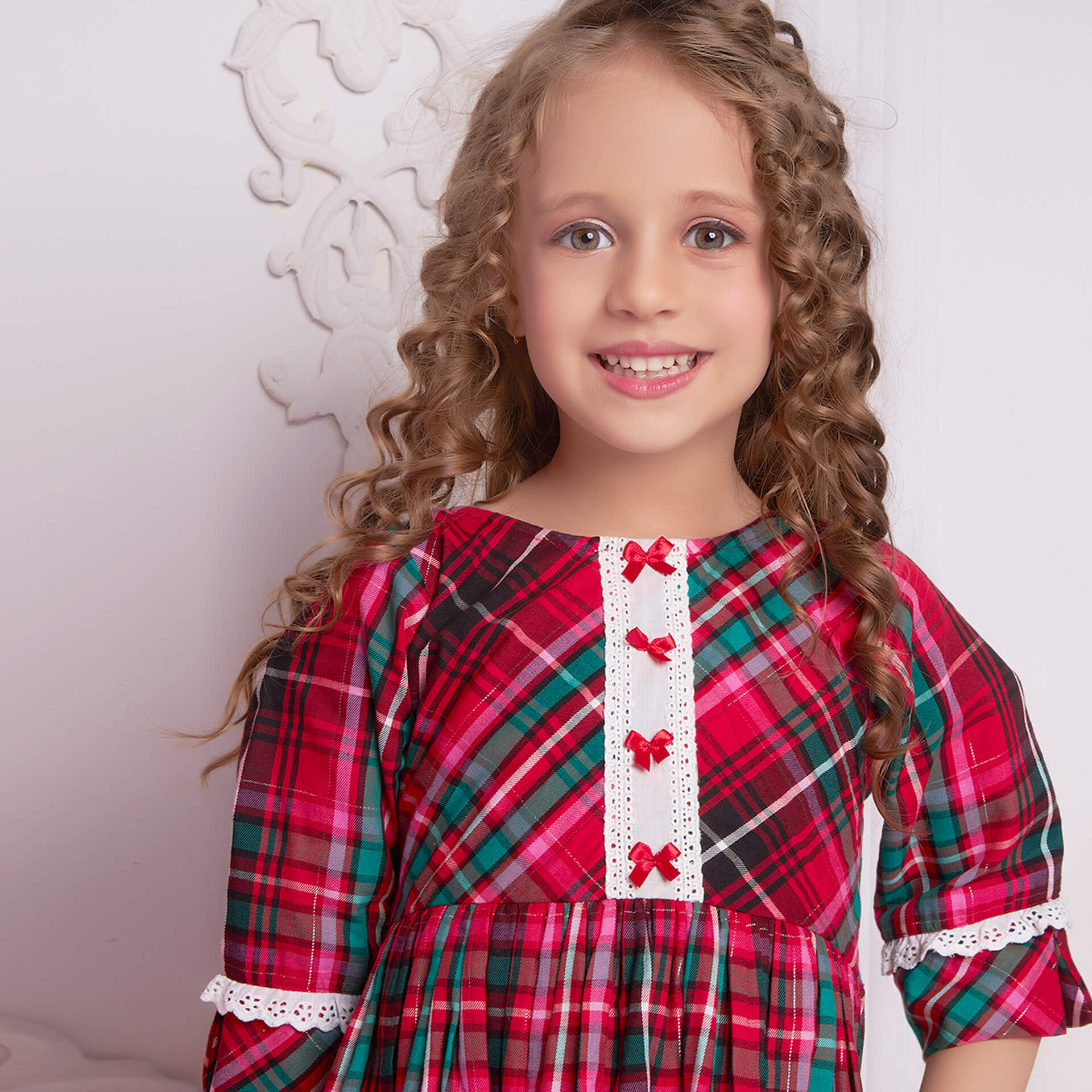 Close-up of a happy little girl in a pink plaid dress with lace and satin bows