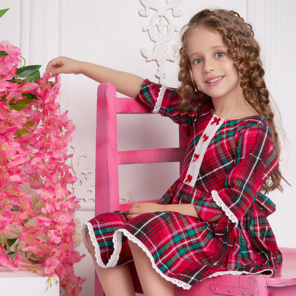 A little girl seated wearing red plaid dress with white lace and red satin bows as trims