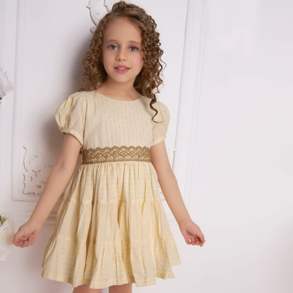 A curly-haired girl wearing an ivory beads dress with gold metallic lace at the waist