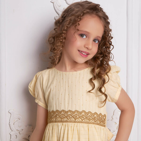 Close-up of a curly-haired girl wearing an ivory beads dress with gold metallic lace at the waist