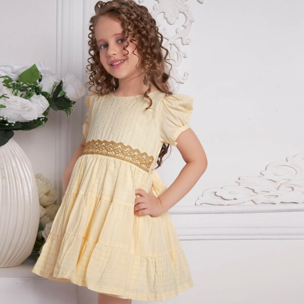 Posing from the side, a little one wears an ivory beads dress with gold metallic lace at the waist