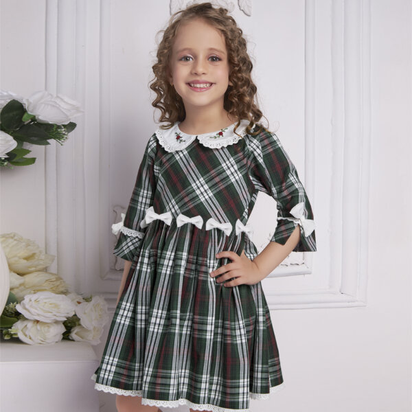 A happy little girl in a green tartan dress with bows at the waist and sleeves adorned with white lace