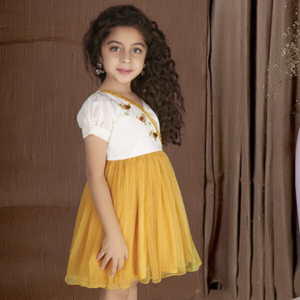Seen from the side a little girl wears mustard bird embroidered dress, featuring sequin embellishments