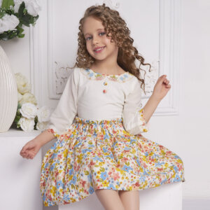A little girl seated wearing ivory floral dress with delicate floral hand-embroidered neckline
