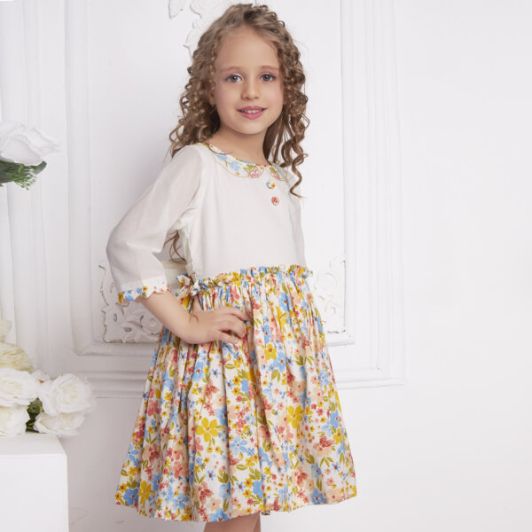 Side pose of a little girl in an ivory floral embroidered dress with decorative cloth buttons