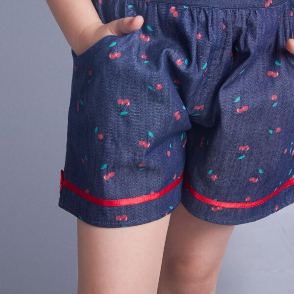 Close-up of navy blue cherry printed shorts featuring satin ribbon bows, with hands inserted into the pockets
