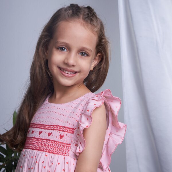 Close up of a smiling girl in pink heart embroidered smock dress