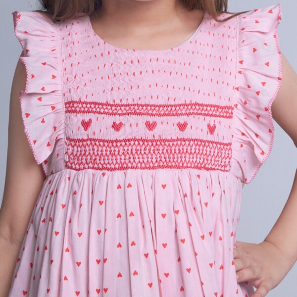 A young girl wears pink heart embroidered smock dress
