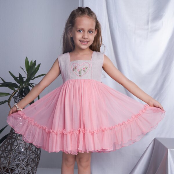 Posing in a peach heart embroidered dress, the girl playfully stretches the skirt with both hands
