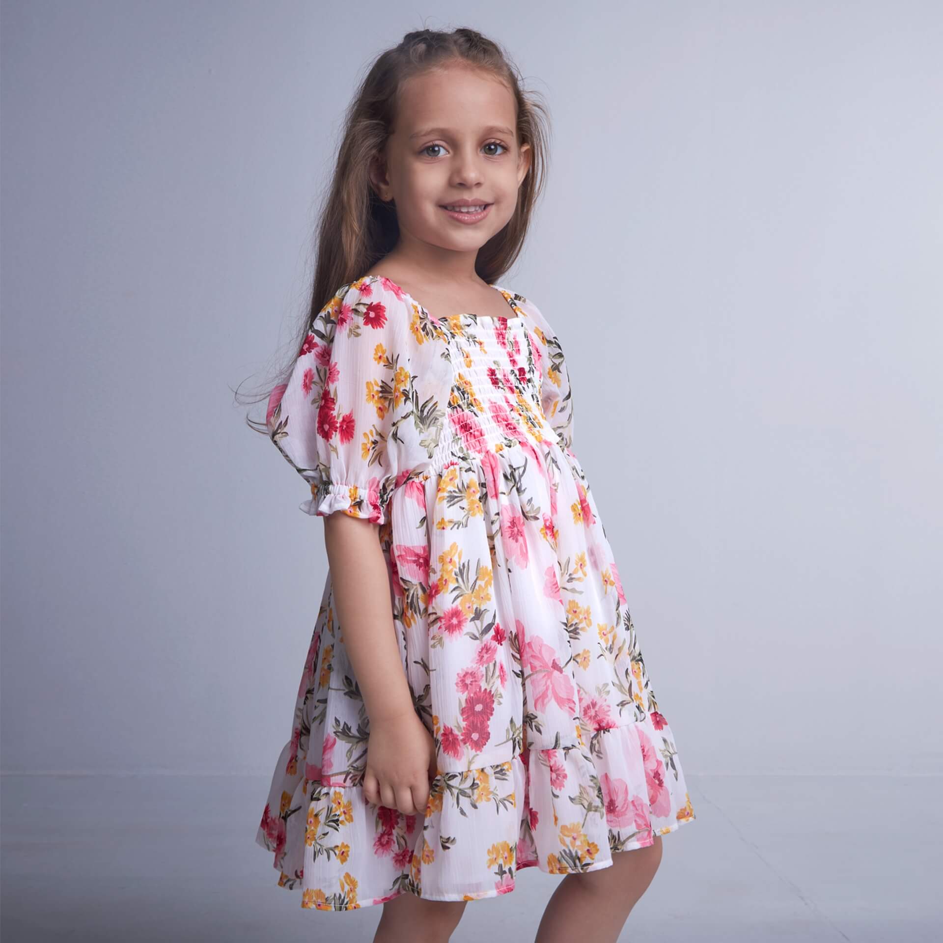 Side view of a girl in white floral printed elasticated dress with hem ruffle