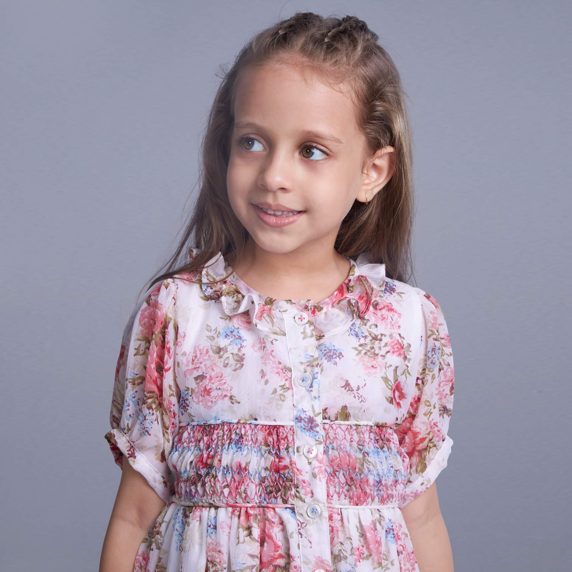 Sweet smile on her face, a little girl wearing an ivory chiffon floral embroidered smock dress