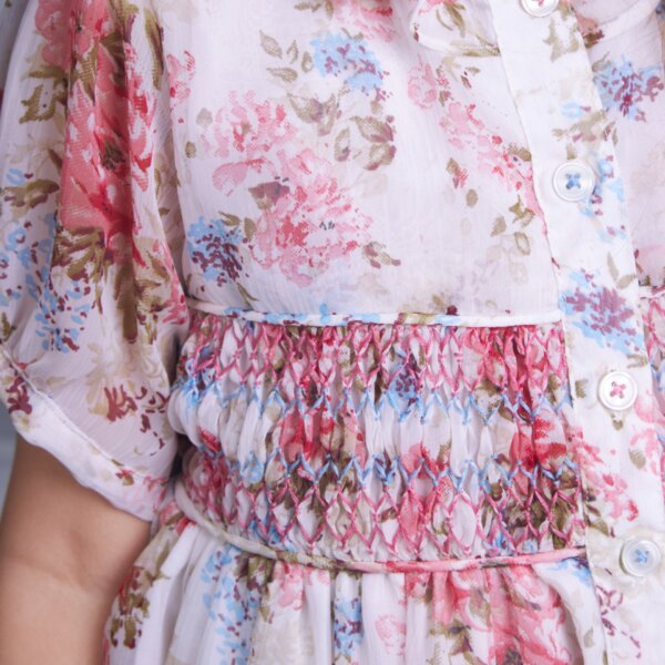 Detailed close-up of an ivory floral smock dress fastened by decorative buttons.