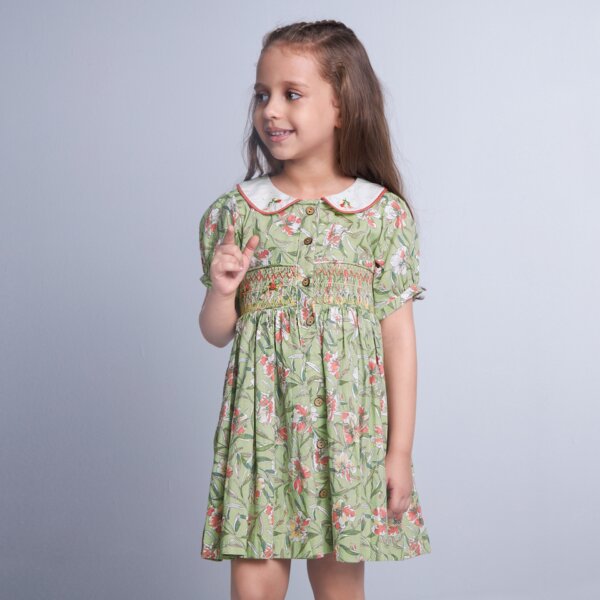A child stands in a green floral smock dress, adorned with delicate hand-embroidered details on the collar