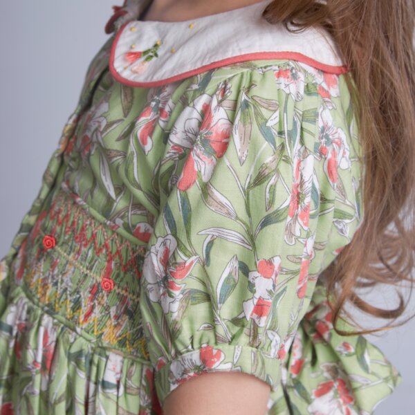 Close-up side view of a girl in a green floral smock dress, adorned with smocking at the waist and hand-embroidered details on the collar.