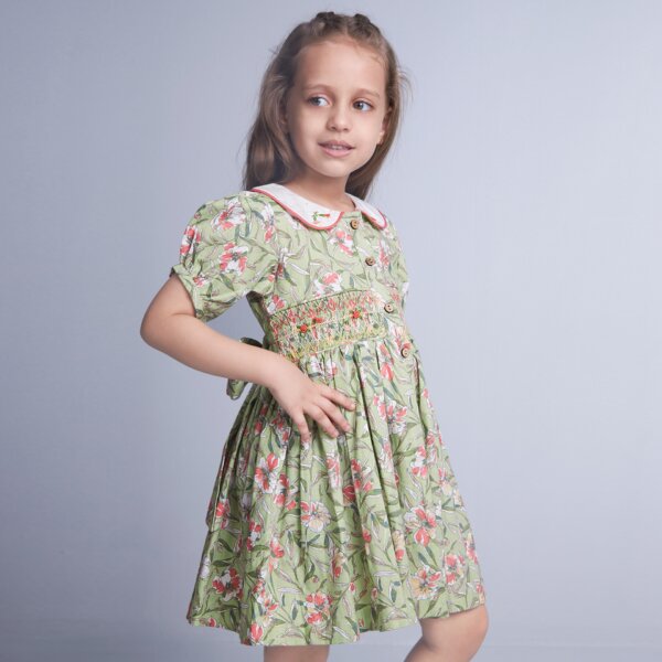 From the side, a girl dressed in green floral smock garment with embroidered collar