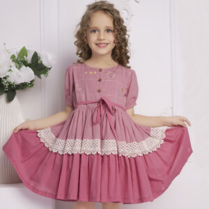 Posing in a pink ombre embroidered dress, the girl playfully stretches the skirt with both hands