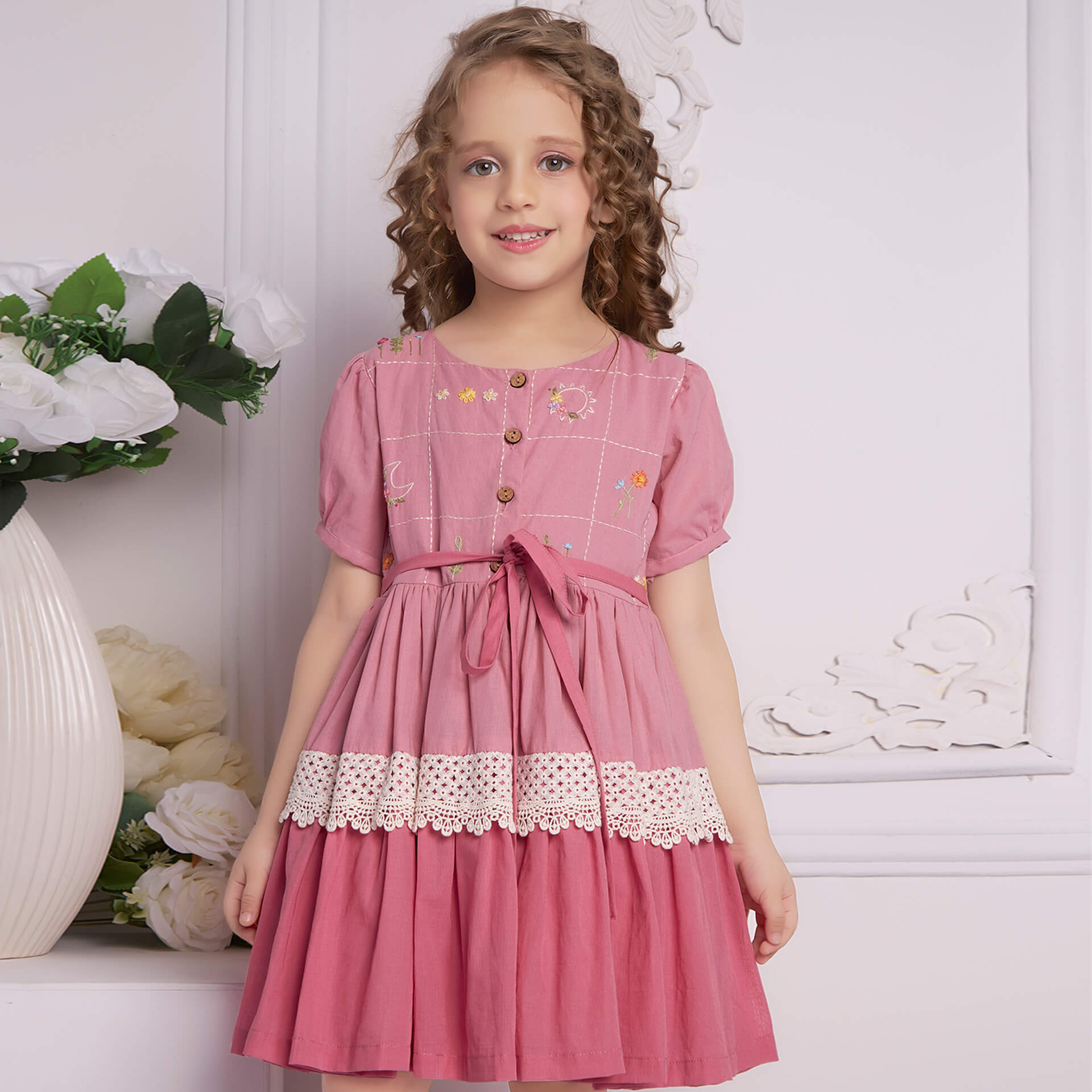 A curly haired girl posing in pink ombre embroidered dress