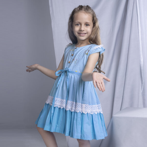 A side view of a young girl in a blue ombre dress, showcasing delicate embroidery and lace details