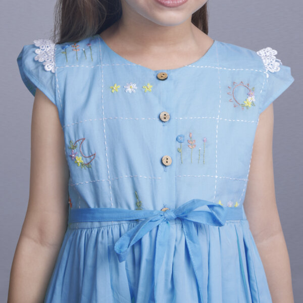 Closeup of hand embroidery on a blue ombre dress with front wood buttons and a tie-up sash