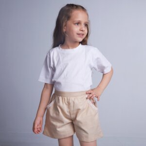 A little girl in cotton tan shorts, designed with a delicate touch of lace trims and hand embroidery on the pocket
