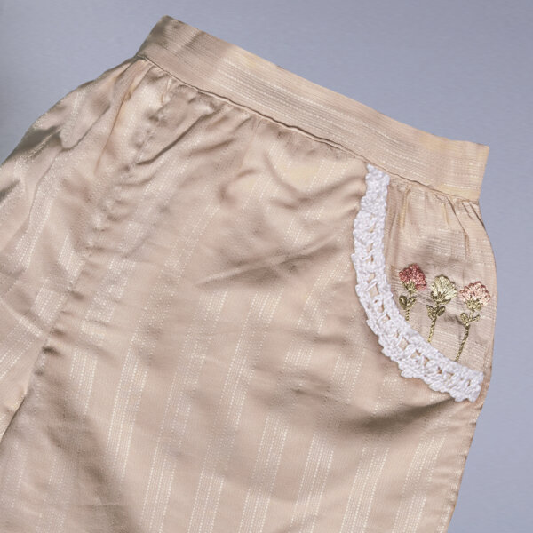 Flat lay of a tan hand embroidered shorts with dual side pockets and lace trims
