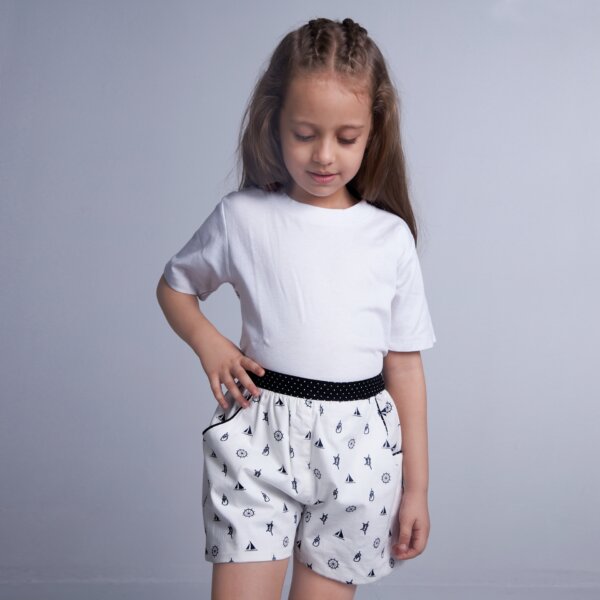 A girl wears white boat printed shorts featuring dual side pockets, elasticated waist, and black dotted fabric trims