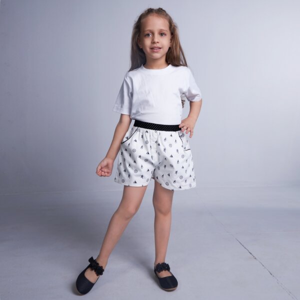 A girl wears white boat printed shorts featuring dual side pockets, elasticated waist, and black dotted fabric trims