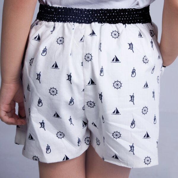 Back view of a girl wears a white boat printed shorts featuring dual side pockets, elasticated waist, and black dotted fabric trims