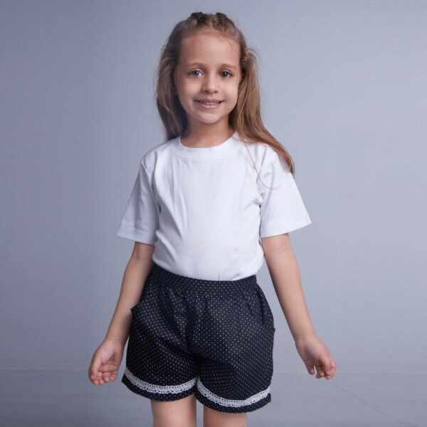 A girl wears dot printed black shorts featuring dual side pockets, elasticated waist and white lace trims