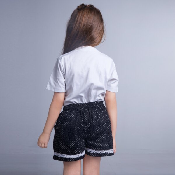 Back view of a little girl stands in a black dot printed shorts with white lace trims