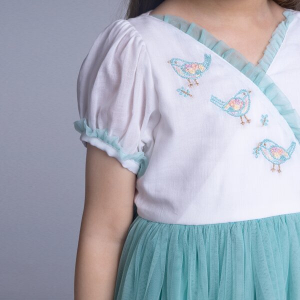 Close-up of bird embroidery in pastel tones on an aqua crossover tulle dress