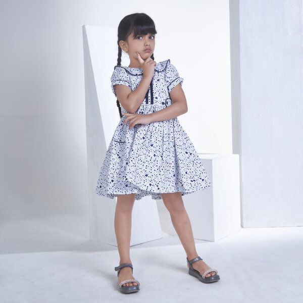 A girl poses in a white floral printed collared dress with adjustable side tabs