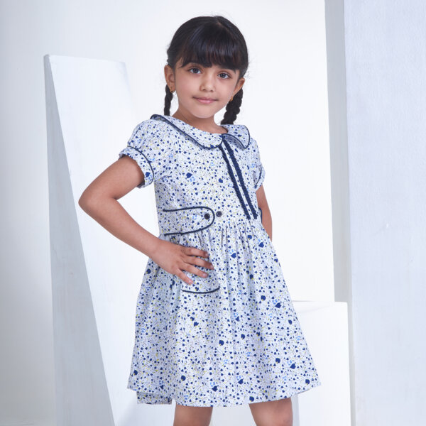 Posing from the side, a girl wears white floral printed collared dress with an adjustable belt at the waist