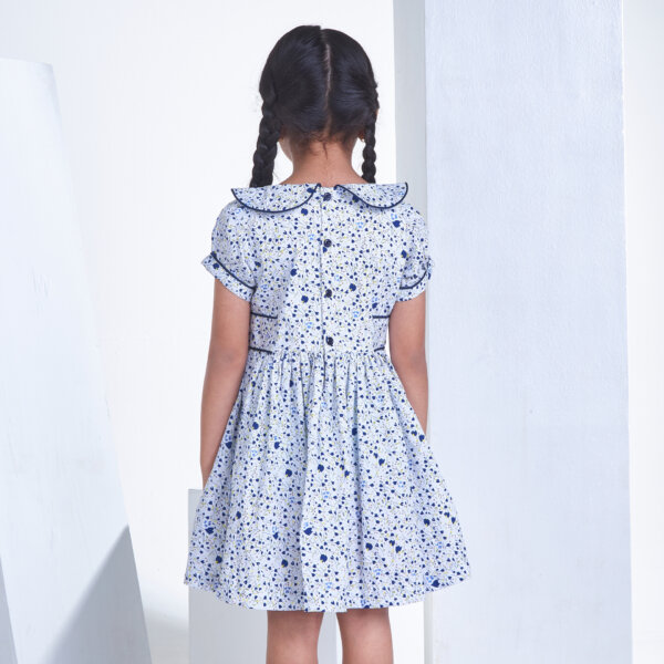 Back view of a girl dressed in a white floral printed collared garment with adjustable side tabs