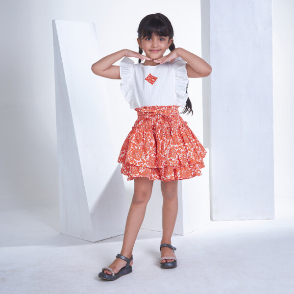 In an ivory embroidered blouse and orange floral printed skirt, a girl strikes a pose with her hands on her chin