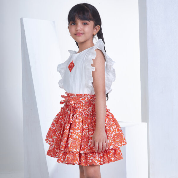 From the side, a girl in an ivory embroidered blouse and orange floral printed high waist skirt