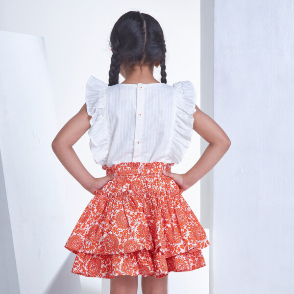 Back view of a girl dressed in an ivory embroidered blouse and orange floral printed high waist skirt