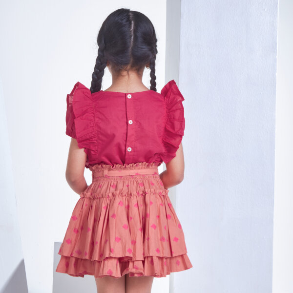 Back view of a girl dressed in pink embroidered ruffle blouse and peach floral printed high waist skirt