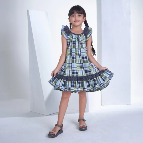 Posing in patch printed fabric dress in tones of navy, turquoise and green, the girl playfully stretches the skirt with both hands