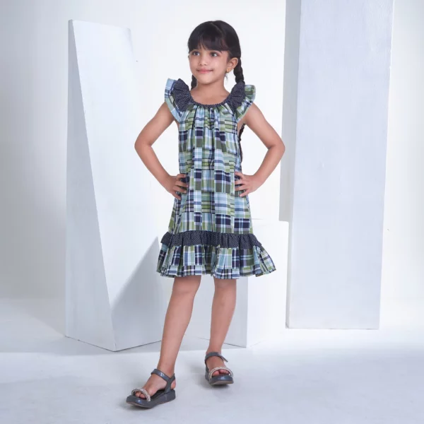 With hands on hips, a little girl stands in a patch printed fabric dress in tones of navy, turquoise and green