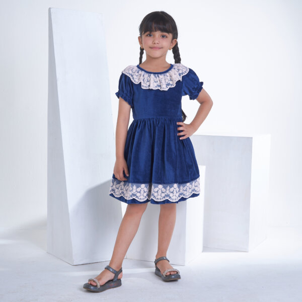 With hands on hips, a little girl stands in a navy velvet dress adorned with white lace