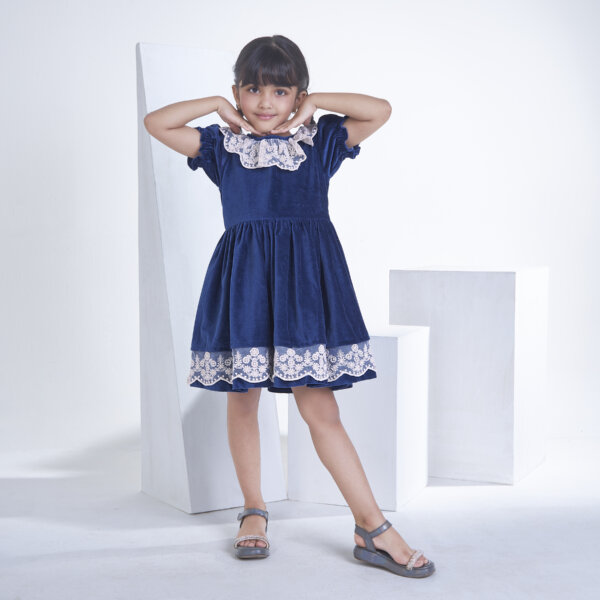A little girl dressed in Navy velvet dress adorned with white lace, with a smiling pose