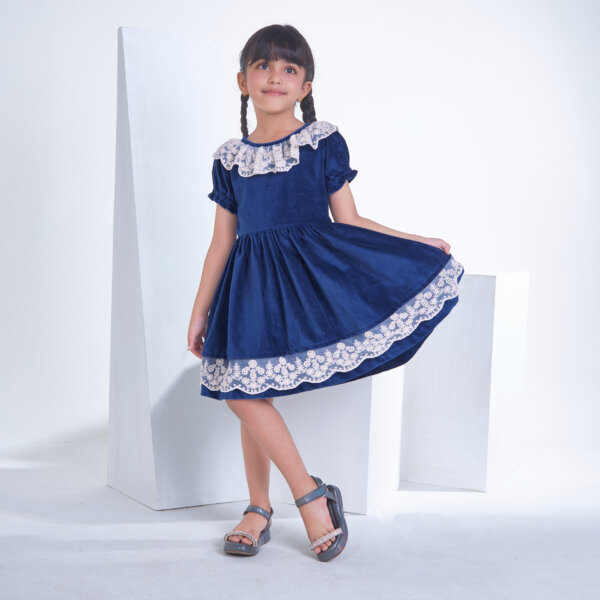 Posing in a Navy velvet dress, the girl playfully stretches the skirt