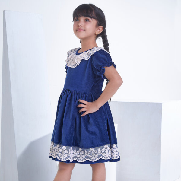 Posing from the side, a little one wears a Navy velvet dress adorned with white lace