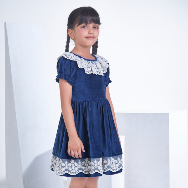 Posing from the side, a little one wears a Navy velvet dress adorned with white lace