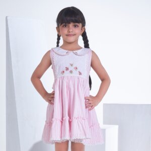 With hands on hips, a little girl stands in a pink striped embroidered collared dress