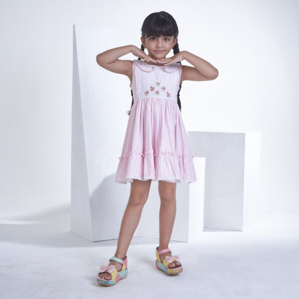 A girl posing in pink striped embroidered collared dress adorned with ruffled hem